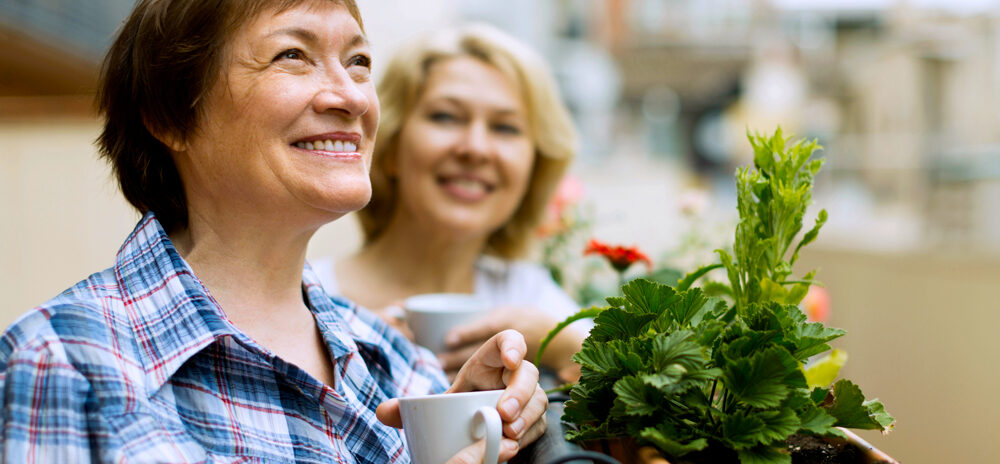 Two woman stood outside with cups of coffee.