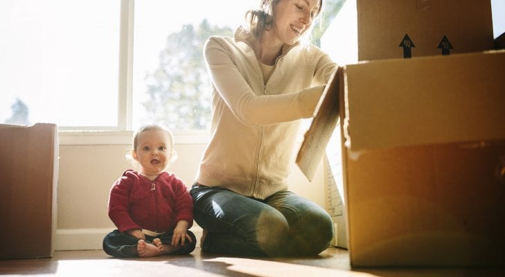 Woman packing cardboard boxes on the floor with a small child sat next to her.