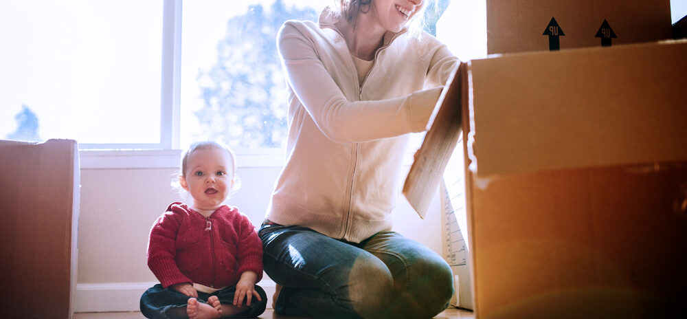 Woman packing a box with a small child next to her.